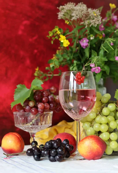 Wine, cheese, fruit and flowers on a table. Vibrant colors of fresh berries and grapes. Colorful still life with glass of pink wine, red and white grapes, gorgonzola cheese and red currant. 