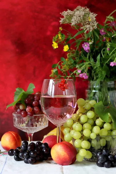 Glass of pink wine, grapes, berries and flowers on a table. Delicious summer food close up photo. Textured background with copy space.