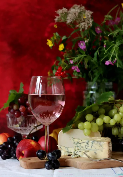 Wine, cheese, fruit and flowers on a table. Vibrant colors of fresh berries and grapes. Colorful still life with glass of pink wine, red and white grapes, gorgonzola cheese and red currant. 