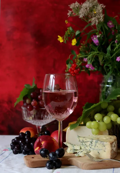 Glass of pink wine, grapes, berries and flowers on a table. Delicious summer food close up photo. Textured background with copy space.