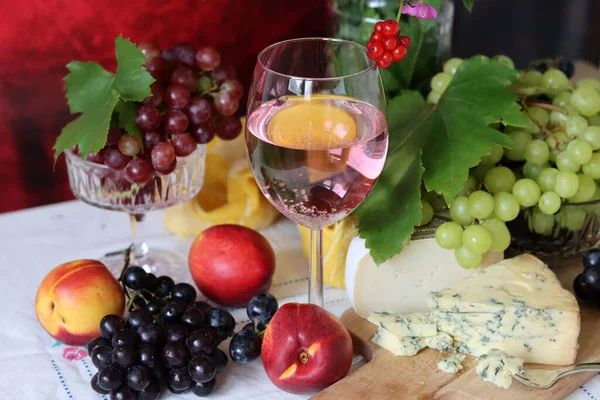 Glass of pink wine, grapes, berries and flowers on a table. Delicious summer food close up photo. Textured background with copy space.