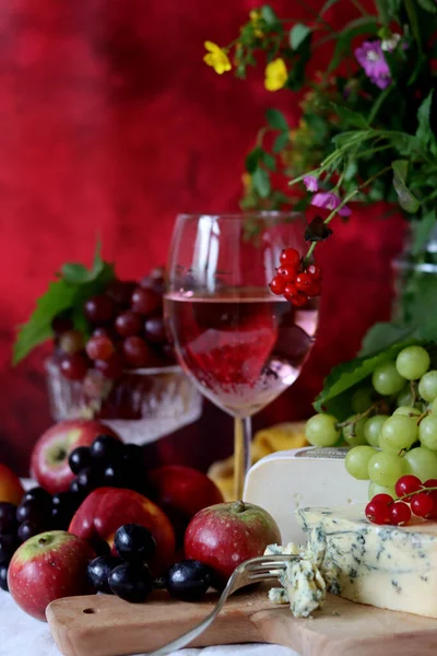 Camembert cheese, green and black grapes, glass of rose wine on a table. Colorful summer still life with seasonal fruit and berries. 
