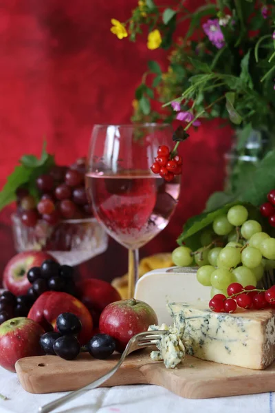 Glass of pink wine, grapes, berries and flowers on a table. Delicious summer food close up photo. Textured background with copy space.