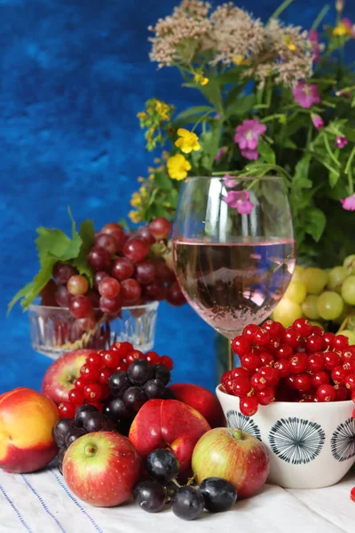 Glass of pink wine, grapes, berries and flowers on a table. Delicious summer food close up photo. Textured background with copy space.