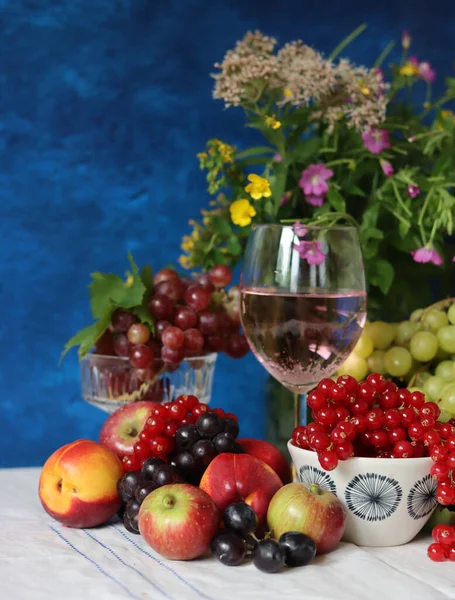 Glass of pink wine, grapes, berries and flowers on a table. Delicious summer food close up photo. Textured background with copy space.