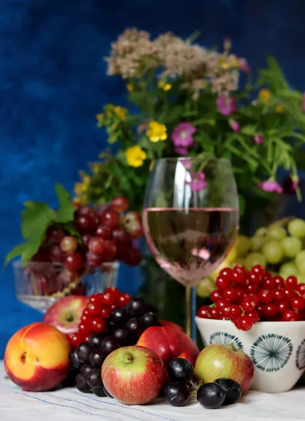Glass of pink wine, grapes, berries and flowers on a table. Delicious summer food close up photo. Textured background with copy space.