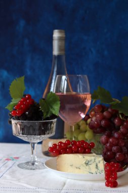 Still life with wine and grapes. Colorful photo of bottle of rose wine and different sorts of grapes. Seasonal fruit on a table. 