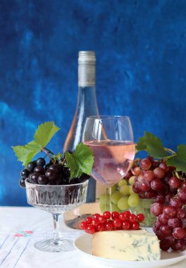 Still life with wine and grapes. Colorful photo of bottle of rose wine and different sorts of grapes. Seasonal fruit on a table. 