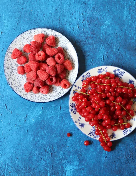 Red currant and raspberry on ceramic plates. Natural vitamins and anti oxidants. Blue textured background with copy space.