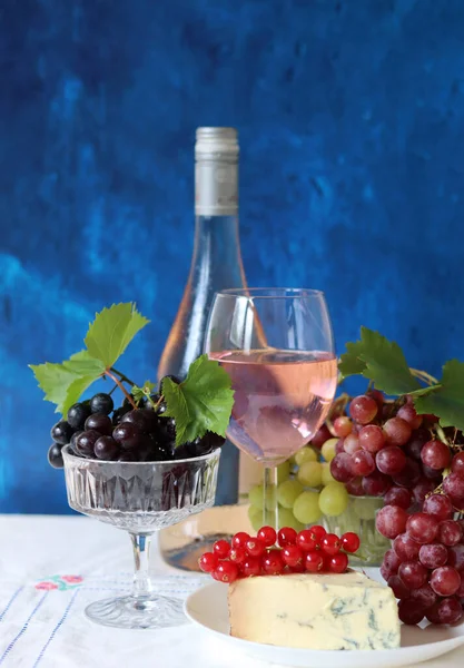 Still life with wine and grapes. Colorful photo of bottle of rose wine and different sorts of grapes. Seasonal fruit on a table.