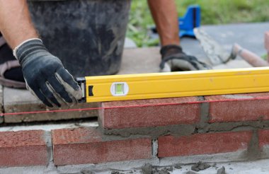 Male hands in protective gloves holding red bricks. Construction worker builds masonry.  Brickwork close up photo. 