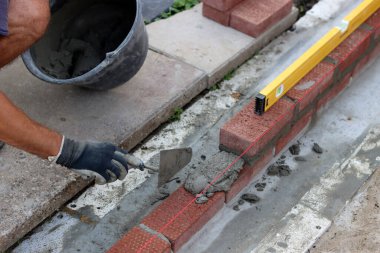 Construction work in progress. Male builder working with red bricks. Masonry wall close up photo.  