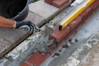 Male hands in protective gloves holding red bricks. Construction worker builds masonry.  Brickwork close up photo. 