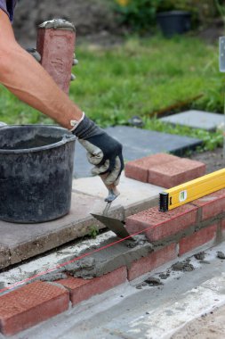 Construction work in progress. Male builder working with red bricks. Masonry wall close up photo.  