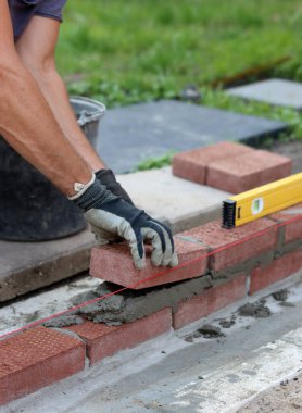 Construction work in progress. Male builder working with red bricks. Masonry wall close up photo.  