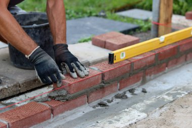 Construction work in progress. Male builder working with red bricks. Masonry wall close up photo.  