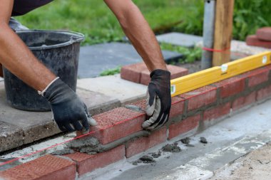 Construction work in progress. Male builder working with red bricks. Masonry wall close up photo.  