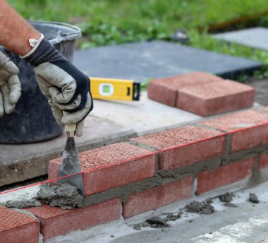 Construction work in progress. Male builder working with red bricks. Masonry wall close up photo.  
