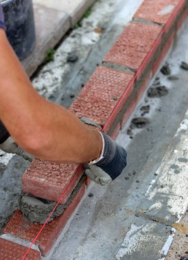 Male hands in protective gloves holding red bricks. Construction worker builds masonry.  Brickwork close up photo. 