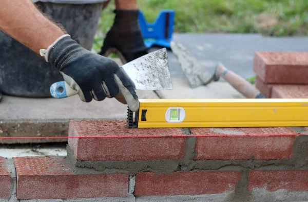 Construction work in progress. Male builder working with red bricks. Masonry wall close up photo.