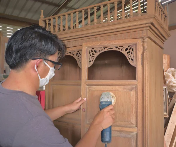 Azjata Trzymający Szlifierkę Elektryczną Zabytkową Drewnianą Szafkę Szorujący Drewno Wewnątrz — Zdjęcie stockowe