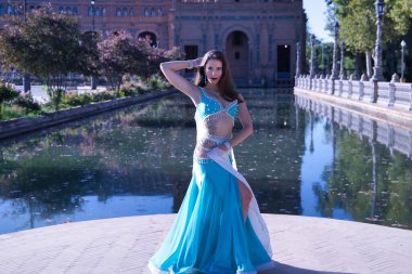 Orta yaşlı, turkuaz elbiseli, yapay elmaslı İspanyol kadın, beyaz peçeli göbek dansı. Göbek dansı konsepti.