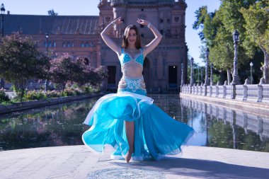 Orta yaşlı, turkuaz elmaslı İspanyol kadın, göbek dansı yaparken elbisesini kaldırıyor. Göbek dansı konsepti.