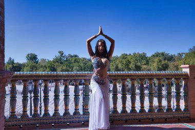 Orta yaşlı İspanyol bir kadın, elmaslı beyaz bir elbise giyiyor, göbek dansı yapıyor, fayans korkuluklarının yanında dans ederken figürler yapıyor. Göbek dansı konsepti.