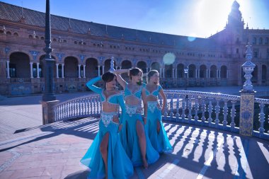 Turkuaz kostümlü ve yapay elmaslı üç orta yaşlı İspanyol kadın göbek dansı yapmak için ellerini kafalarının arkasına koyup güneş ışınlarını alıyorlardı. Göbek dansı konsepti.