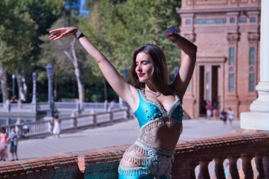 Orta yaşlı İspanyol kadın, turkuaz kostüm ve yapay elmaslar giyiyor, göbek dansı için, taş bir balerin yanında dans ederken figürler yapıyor. Göbek dansı konsepti.