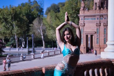 Orta yaşlı İspanyol kadın, turkuaz kostüm ve yapay elmaslar giyiyor, göbek dansı için, taş bir balerin yanında dans ederken figürler yapıyor. Göbek dansı konsepti.