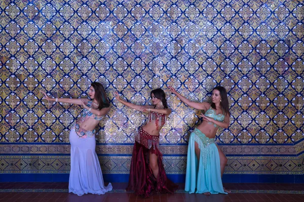 Orta yaşlı, güzel renkli ve boncuklu elbiselerle göbek dansına giden üç İspanyol kadın, arka planda güzel fayanslardan oluşan bir duvarla dans ederken figürler yapıyorlar. Göbek dansı konsepti.