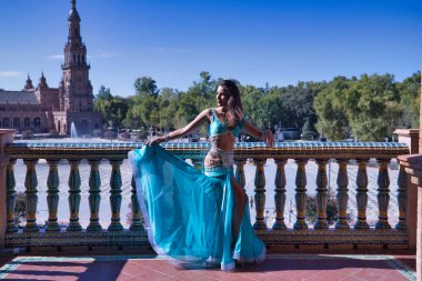 Orta yaşlı İspanyol kadın, turkuaz elbise ve elmaslar giyiyor, göbek dansı için, fayansların yanında dans ederken figürler yapıyor. Göbek dansı konsepti.