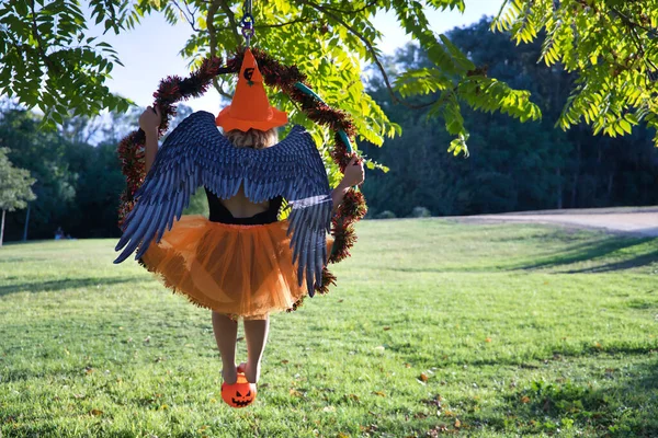 오렌지 모자와 치마를 호박을 날개를 나무에 매달려 공중의 금발의 할로윈 — 스톡 사진
