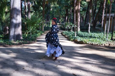 Genç bayan flamenko sanatçısı, Latin ve esmer, tipik siyah flamenko dans takımı ile beyaz benekli, toprak bir yolda koşuyor. Flamenko konsepti, dansçı, tipik İspanyol dansı..