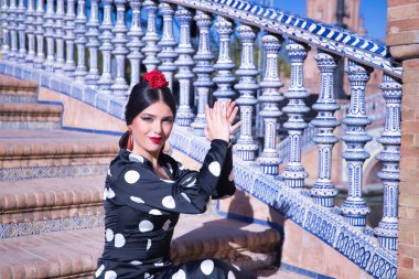 Genç bayan flamenko sanatçısı, İspanyol ve esmer, tipik beyaz benekli siyah flamenko dans takımı, merdivende oturuyor, avuç içi oynuyor. Flamenko konsepti, dansçı, tipik İspanyol dansı..