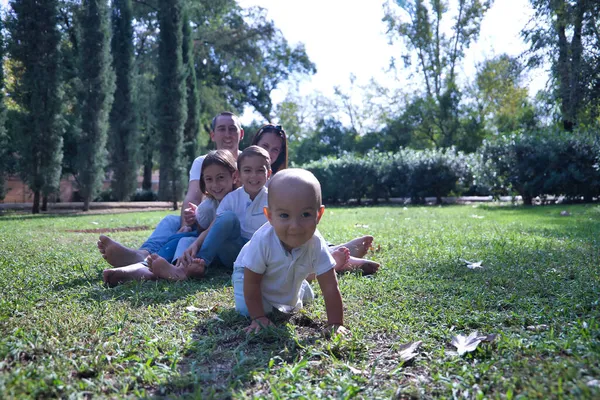 幸せなことに 5つの公園の芝生の上に座っての大家族として 彼らは若い1つの距離クロールを見て笑っている コンセプトファミリー大家族幸福第一歩這う — ストック写真