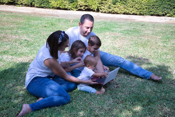 幸せなことに 5つの芝生の上に公園のタブレットを見て座っての大家族 3人の子供と そのうちの1人は性転換した女の子です コンセプト技術 タブレット 子供の頃の性転換 — ストック写真