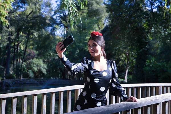 若い女性フラメンコアーティスト ブルネット 白い水玉と典型的な黒フラメンコダンススーツで 彼女の携帯電話で自撮りを取ります フラメンコのコンセプト 自撮り ダンサー 典型的なスペイン舞踊 — ストック写真