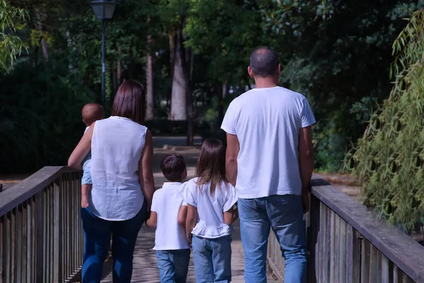 Happy, large family of five seen from the back, walking on a wooden bridge. Parents with three children, one of them a transsexual girl. Family concept, large family, transsexuality in childhood.