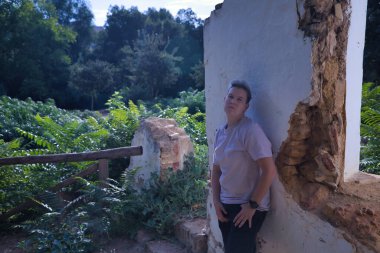 İkili olmayan, ciddi davranışları olan, harap olmuş bir binanın duvarına yaslanan biri. İkili olmayan konsept, lgbtq +, dahil etme, gay, lezbiyen, lgbtq.