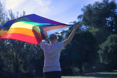 Sırtı dönük, ikili olmayan kişi elleriyle rüzgarda sallanan yeni lgbtq gurur bayrağını kaldırıyor. İkili olmayan konsept, lgbtq +, dahil etme, gay, lezbiyen, lgbtq.