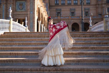 Genç flamenko kadın, İspanyol ve esmer, tipik flamenko dans takımı içinde, merdivenlerde altın çiçeklerle kırmızı manila şalıyla dans ediyor. Flamenko konsepti, dansçı, tipik İspanyol dansı..