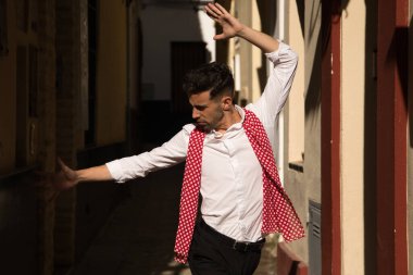 Beyaz gömlekli, siyah pantolonlu, dans ayakkabılı, kırmızı mendilli, dar bir sokakta beyaz benekli bir flamenko dans eden genç bir İspanyol. Sanat, dans, kültür, gelenek.