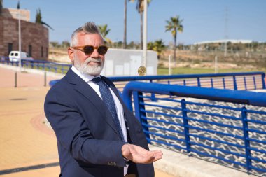 Olgun bir adam, yönetici, gri saçlı, sakallı, güneş gözlüğü takan, ceket ve kravat takan, eliyle havaya kripto para fırlatan. Yönetici kavramı, bitcoin, business, mines.