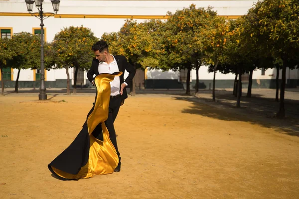 Young Spanish man in black shirt, jacket and pants, with dancing shoes, dancing flamenco with black and gold capote in the street. Typical Spanish concept, art, dance, culture, tradition.