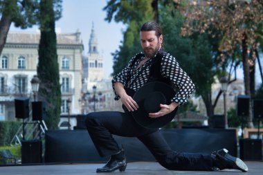 Sakallı, at kuyruklu, siyah tişörtlü, beyaz benekli, siyah pantolonlu ve ceketli, sahnede şapkalı flamenko dansı yapan genç bir adam. Sanat, dans, kültür, gelenek.