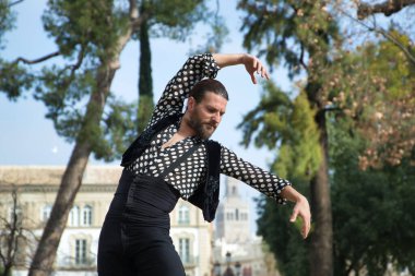 Sakallı, at kuyruklu, siyah tişörtlü, beyaz benekli, siyah pantolonlu ve ceketli, sahnede flamenko dansı yapan genç bir adam. Sanat, dans, kültür, gelenek.