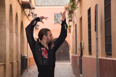 Sakallı, at kuyruklu, siyah şeffaf gömlekli, siyah puantiyeli, kırmızı güllü, siyah pantolonlu ve ceketli, şehirde flamenko dansı yapan genç bir adam. Sanat, dans, kültür, gelenek.