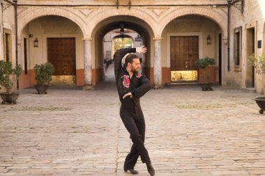 Sakallı, at kuyruklu, siyah şeffaf gömlekli, siyah puantiyeli, kırmızı güllü, siyah pantolonlu ve ceketli, şehirde flamenko dansı yapan genç bir adam. Sanat, dans, kültür, gelenek.